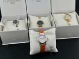 trois montres dans une boîte blanche, avec des bracelets orange, posées sur une table noire