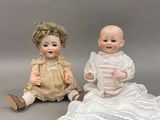 deux poupées en porcelaine assises l'une à côté de l'autre sur une surface grise