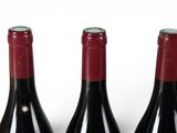 three bottles of red wine are lined up on a white surface