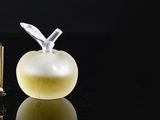 a bottle of perfume next to an apple on a black surface