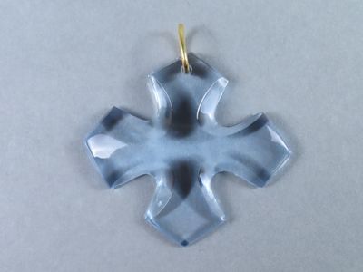 une photo d'un pendentif en forme de croix en verre posé sur une surface blanche