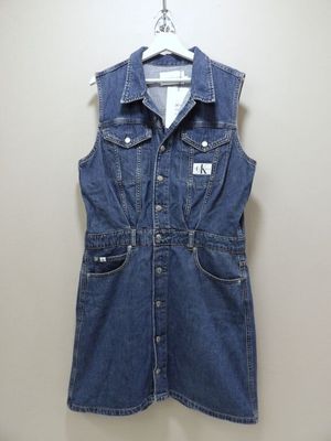 un gilet en jean bleu avec des poches, suspendu à un cintre devant un mur blanc