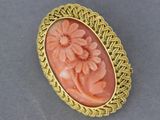 une image représentant une broche aux couleurs or et corail, ornée de fleurs