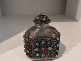un flacon de parfum en verre argenté et turquoise posé sur une table blanche