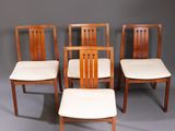 four wooden chairs with white upholstered cushions sit in front of a gray background