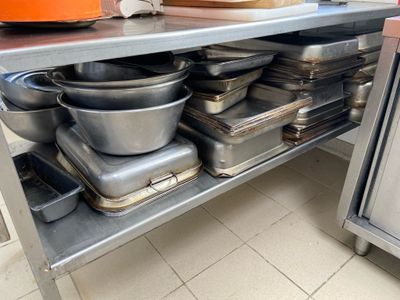 Plusieurs casseroles et poêles sont empilées sur une étagère métallique dans une cuisine.