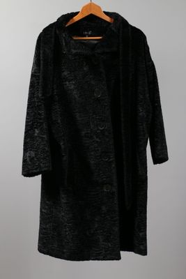 a black coat hanging on a hanger against a white wall