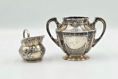 un vase en argent à côté d'un autre vase en argent, posé sur une surface blanche