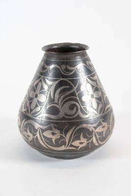 un vase noir et argenté posé sur une surface blanche