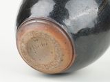 a black vase with a brown lid sitting on a white surface