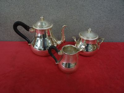 un service à thé et à café en argent composé de trois pièces, posé sur une nappe rouge
