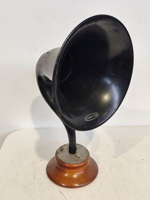 un gramophone noir et argenté posé sur un socle en bois, sur une surface blanche