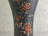 a black vase with red flowers on it sitting on a table