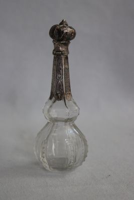 un flacon de parfum ancien en verre, muni d'une poignée en métal, posé sur une surface blanche