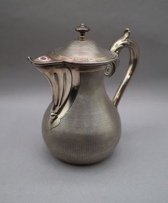 an antique silver coffee pot with a lid on a gray surface
