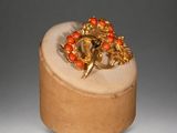 an image of a gold and coral colored broochle on a wooden stand