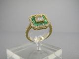 une bague sertie d'une émeraude et de diamants, posée sur un socle en acrylique transparent