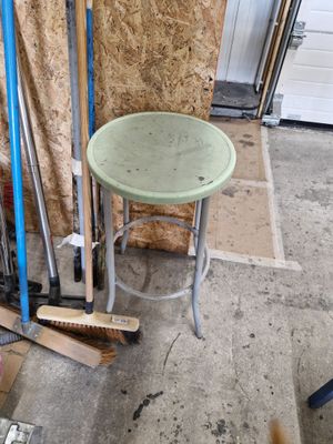 un tabouret vert posé à côté d'une pile de balais