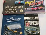 three books on a table with a picture of a race car in the background