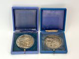 two silver medals in a blue box on a white surface