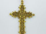 un pendentif en forme de croix en or, orné d'un motif en filigrane sur fond blanc