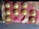 nine gold buttons on a pink piece of paper