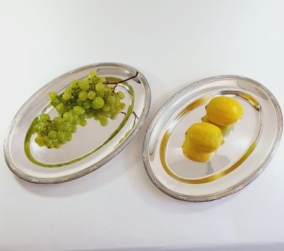 two oval silver trays with lemons and grapes on them