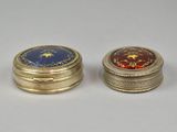 two small gold and enamel boxes on a white surface