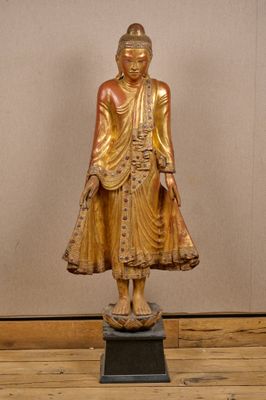 statue d'un Bouddha debout sur un socle, devant un mur beige