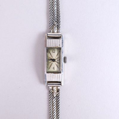 a close up of a watch on a white surface with a chain around it