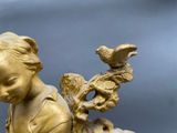 a gold statue of a girl with a bird on her shoulder