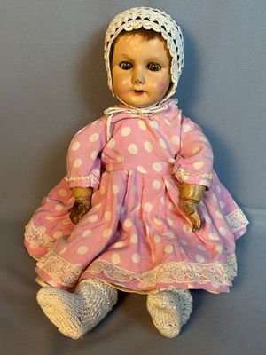 Une vieille poupée vêtue d'une robe rose et d'un bonnet est assise sur une surface grise