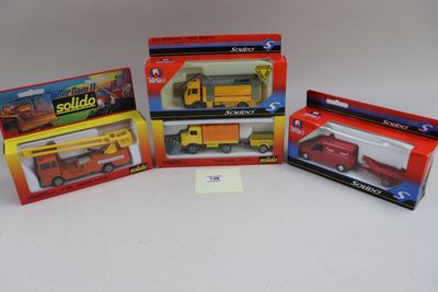 On voit trois camions miniatures dans leur boîte posés sur une surface blanche