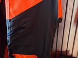 Des sacs à dos orange et noirs sont alignés contre un mur en bois