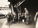 black and white photograph of a group of naked women standing in front of a man