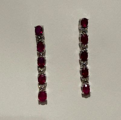 une paire de boucles d'oreilles en rubis et diamants posées sur un fond blanc