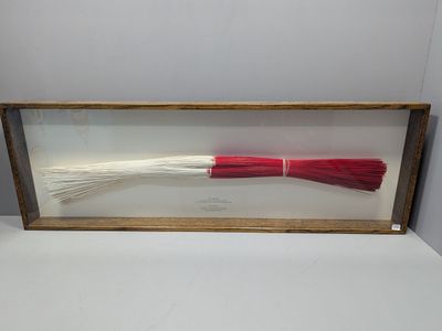 un pinceau rouge et blanc dans un cadre en bois posé sur une surface blanche