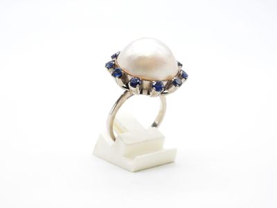 une bague ornée d'une perle blanche et d'un saphir, posée sur un socle en marbre blanc