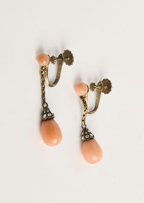 une photo représentant une paire de boucles d'oreilles couleur pêche posées sur une surface blanche