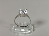 une photo d'une bague en diamant posée sur un socle transparent, sur une surface blanche