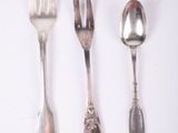 three spoons and a fork are lined up on a white surface
