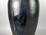 un vase noir posé sur une table, sur fond blanc