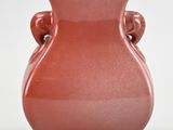 a red vase with two handles sitting on a white surface