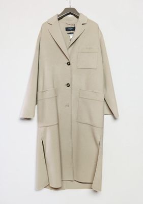 a beige coat hangs on a hanger against a white wall