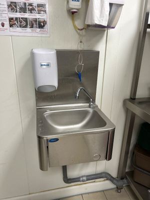 un lavabo en acier inoxydable dans une salle de bains, avec un distributeur de serviettes fixé au mur
