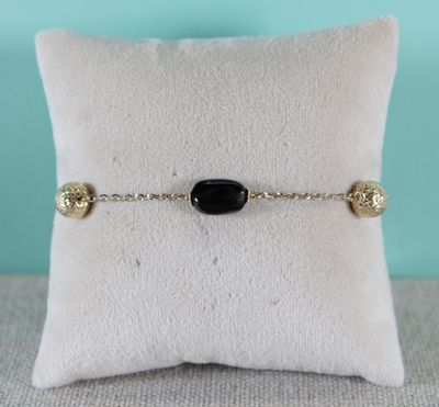un bracelet en pierre noire posé sur un coussin blanc, sur un fond bleu