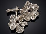 a close up of a silver broochle with flowers on a black surface