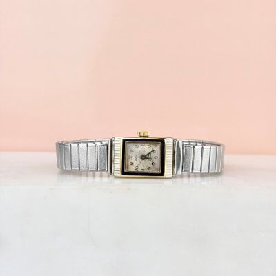 une image représentant une montre argentée et dorée posée sur une surface blanche