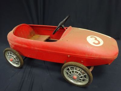 an old red pedal car sitting on top of a black surface