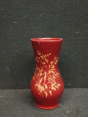un vase rouge orné de motifs dorés, posé sur une surface noire